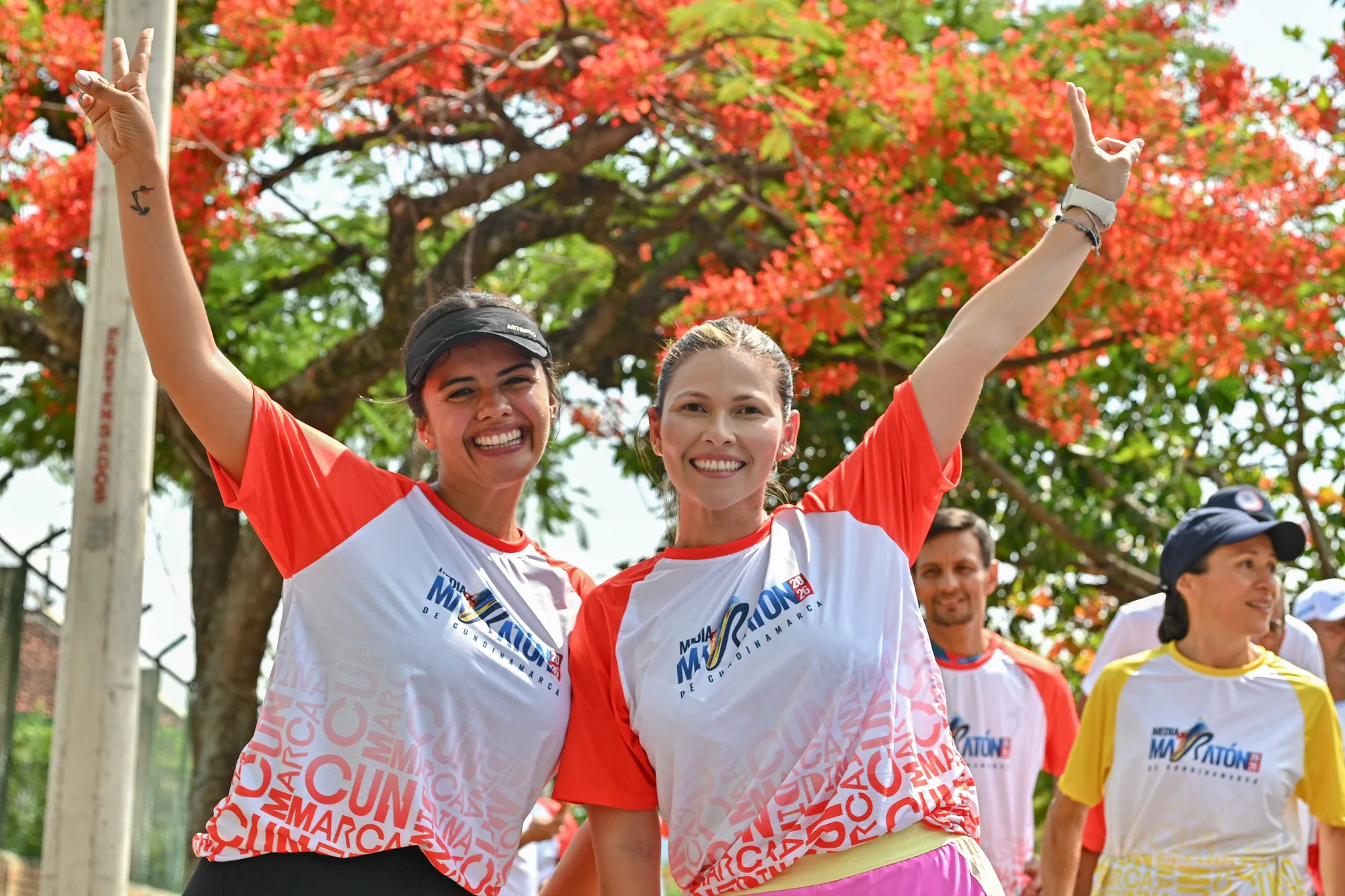 Dos participantes celebrando con los brazos en alto bajo un árbol florecido